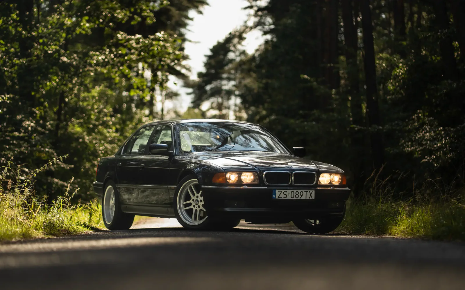 Black BMW 740i E38 with its lights on in a dark forest